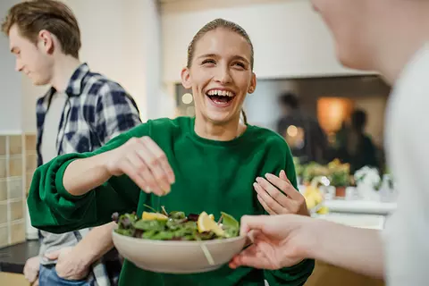 Lachende Frau bereitet einen Salat zu