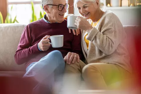 Glückliches älteres Paar mit Tassen in der Hand auf Sofa
