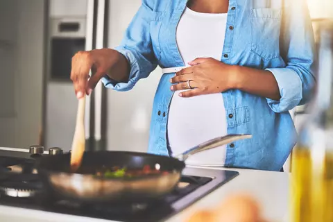Schwangere Frau steht in der Küche und kocht sich etwas Gesundes in einer Pfanne 