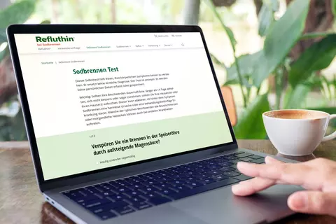 Person vor Laptop mit Kaffeetasse macht Selbsttest bei Sodbrennen
