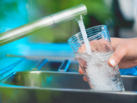 Die Han einer Frau, die ein Glas unter einem laufenden Wasserhahn füllt